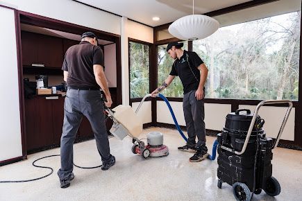 Two men are cleaning a floor with a vacuum cleaner.