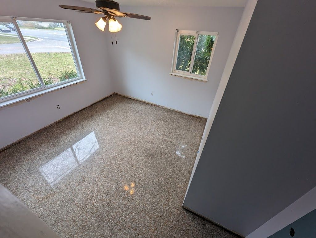 An empty room with a ceiling fan and two windows