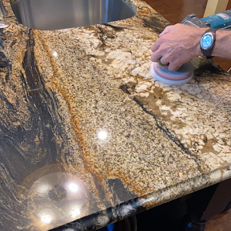 A person is polishing a granite counter top in a kitchen.