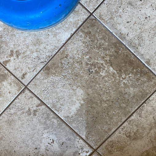 A dirty tile floor with a blue bowl on top of it.