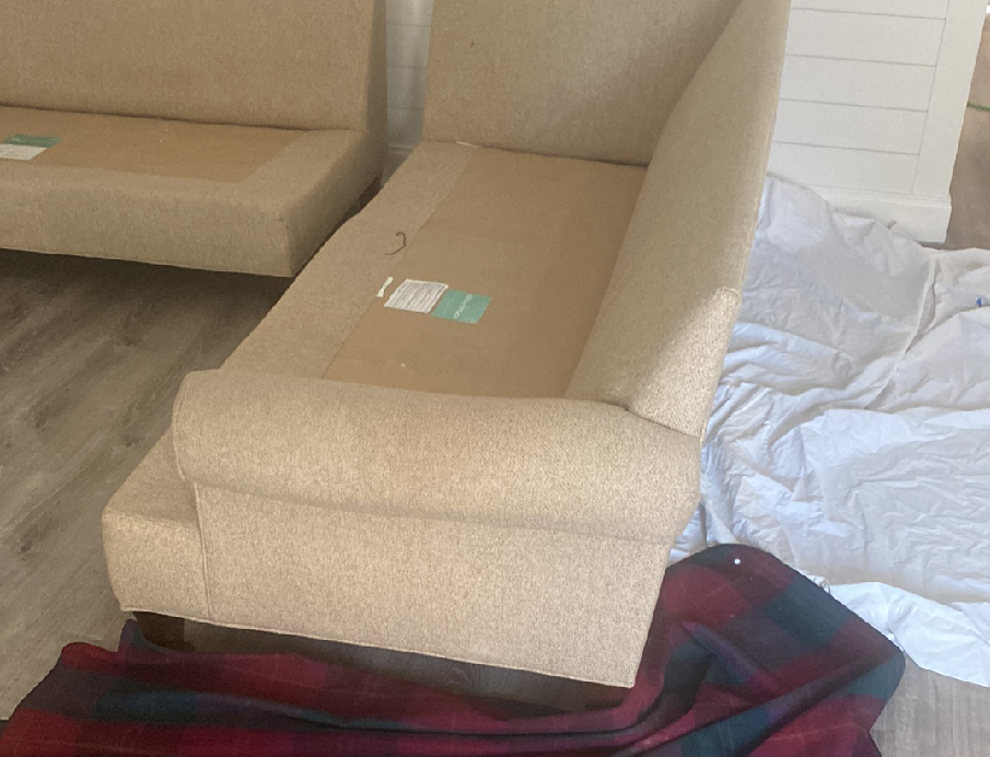 A couch is sitting on the floor next to a plaid blanket.