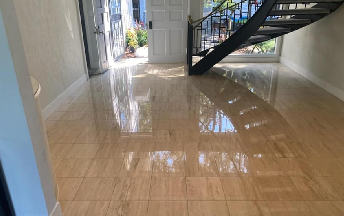 Light-floored hallway with open doorway, staircase, and bright sunlight reflecting on the polished surface.