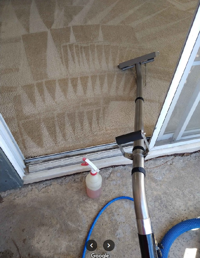 A vacuum cleaner is cleaning a carpet next to a sliding glass door.