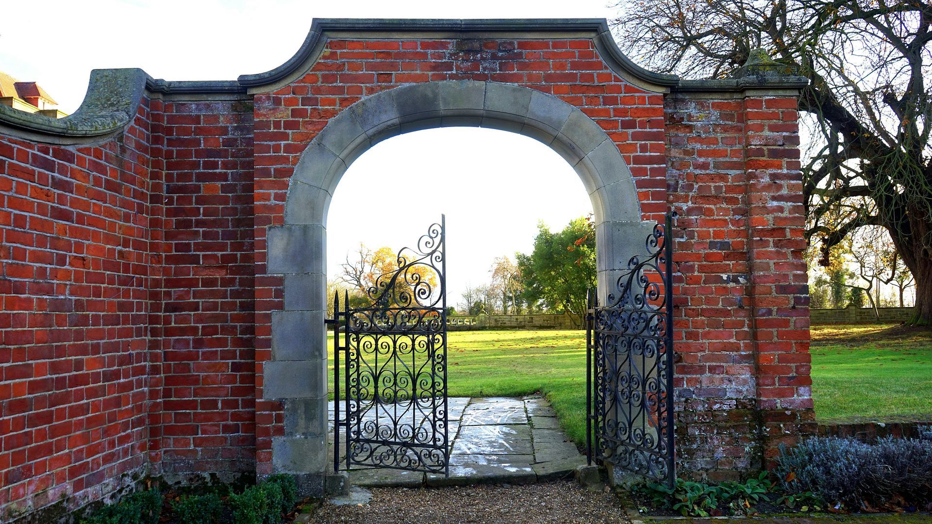 A brick wall with a gate leading to a field.