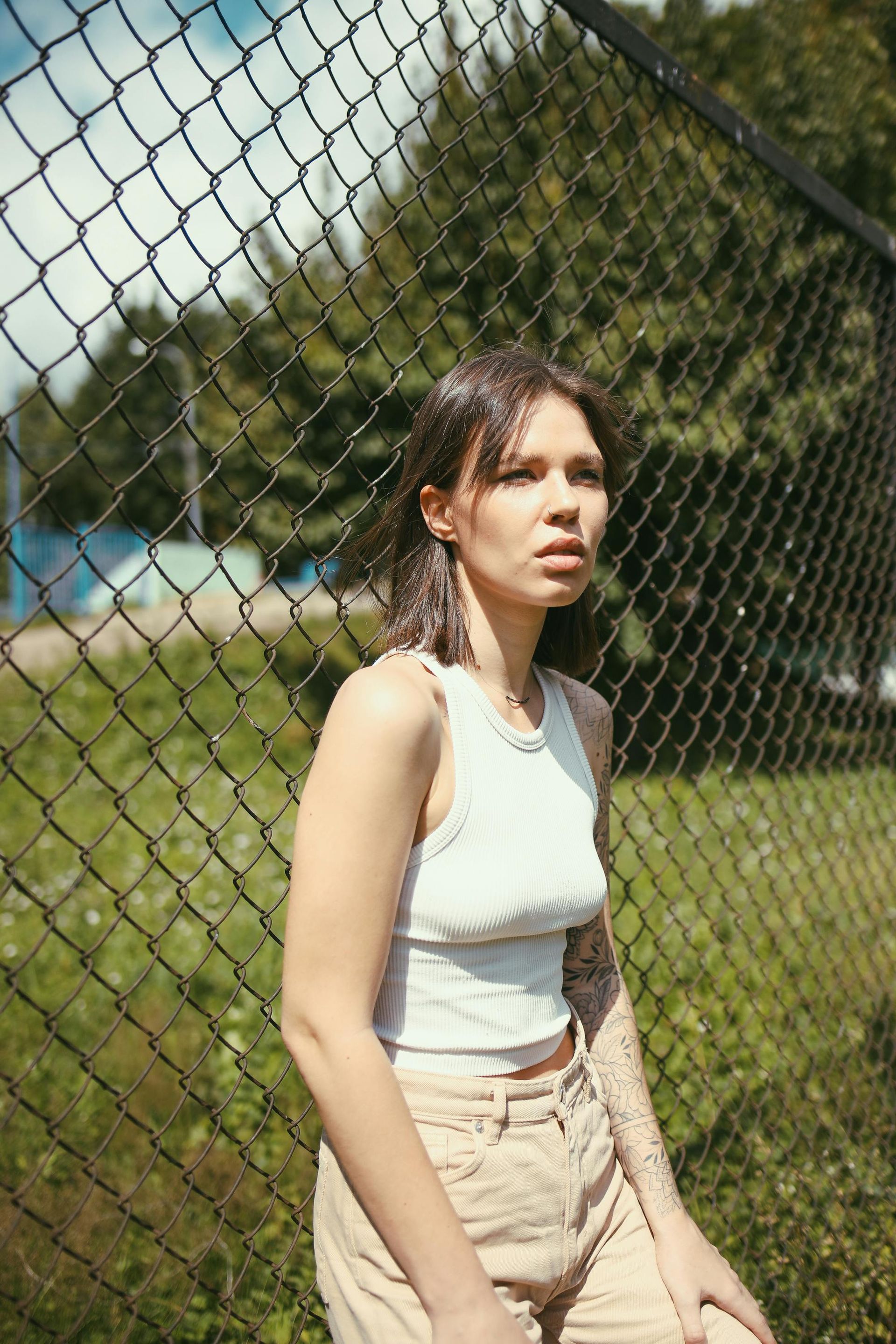A woman is standing in front of a chain link fence.