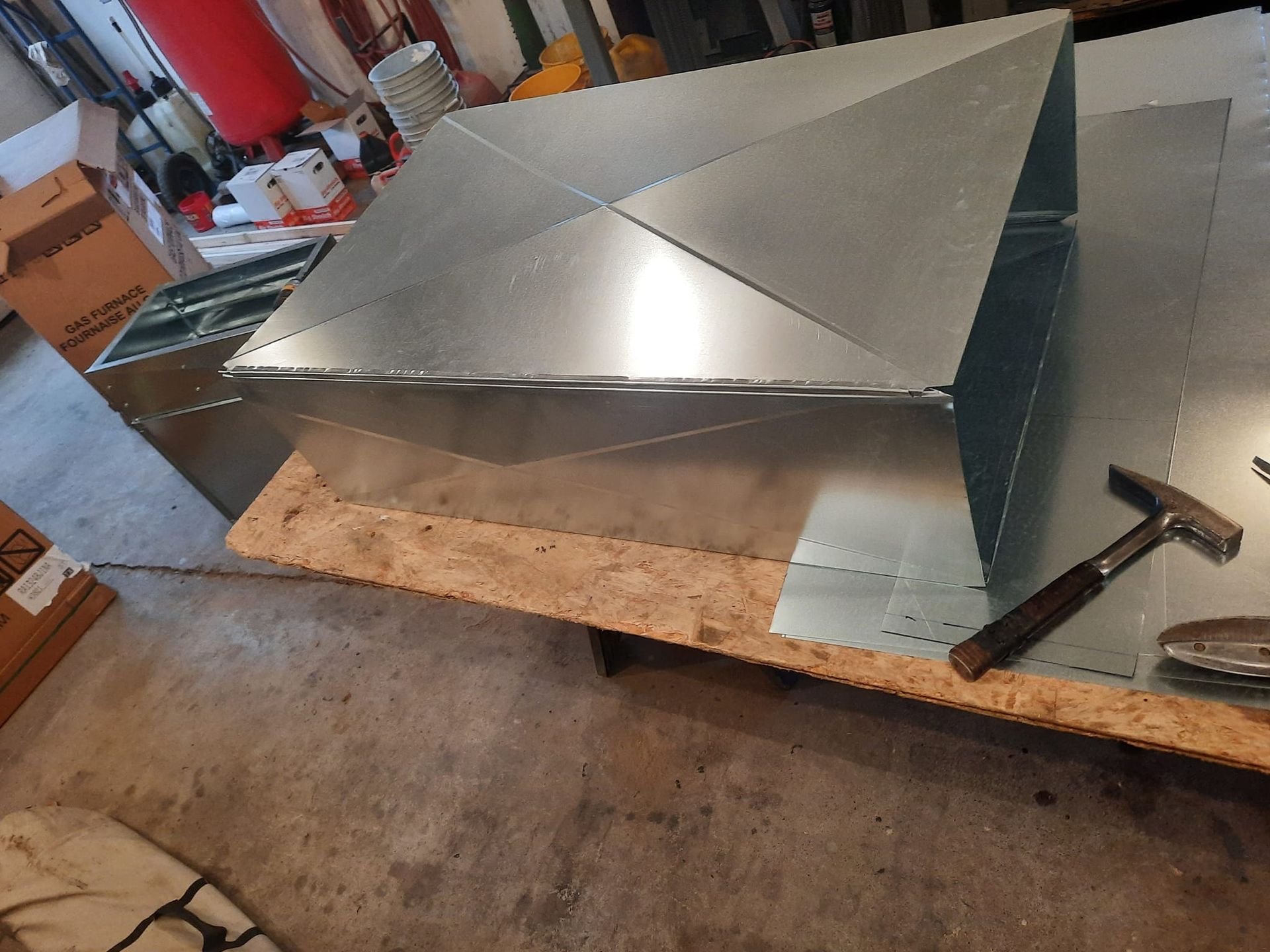 A piece of metal is sitting on a wooden table next to a hammer.