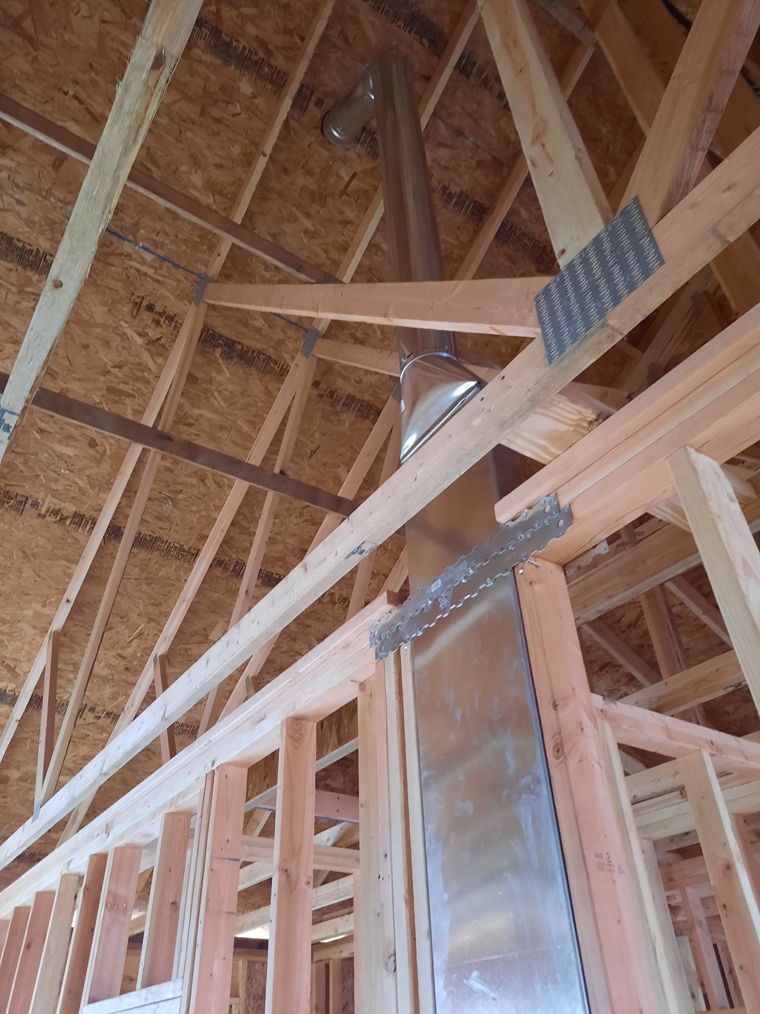 The inside of a house under construction with a metal pipe coming out of the ceiling.