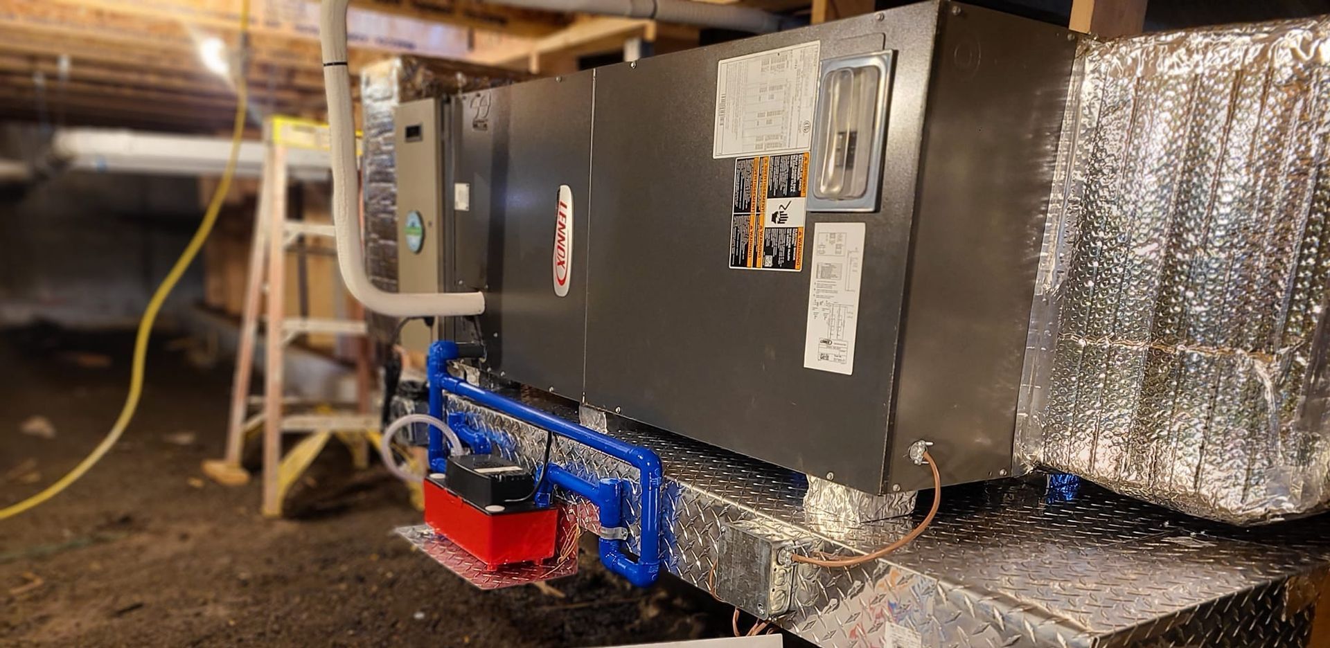 A large air conditioner is sitting in a basement next to a ladder.