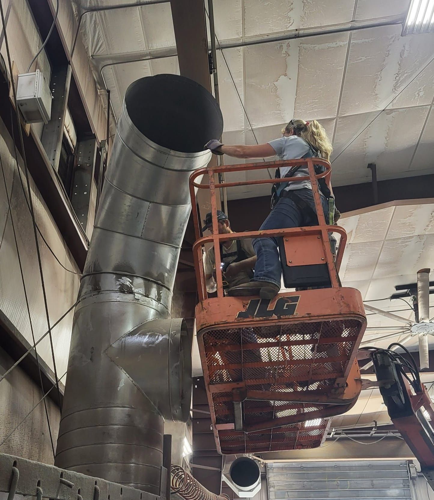 A man is standing on a jlg lift working on a pipe.