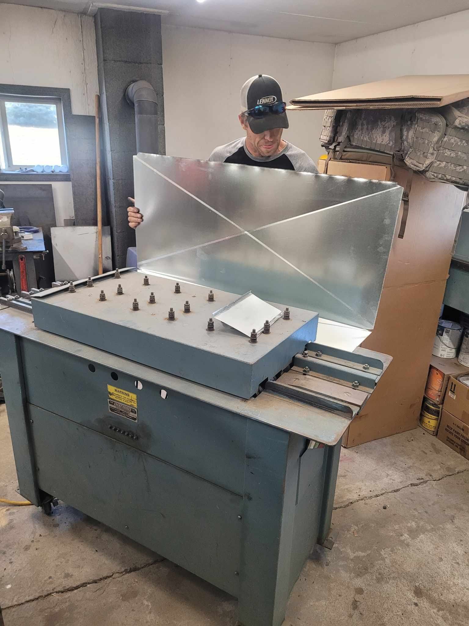 A man is standing in front of a machine in a garage holding a piece of metal.
