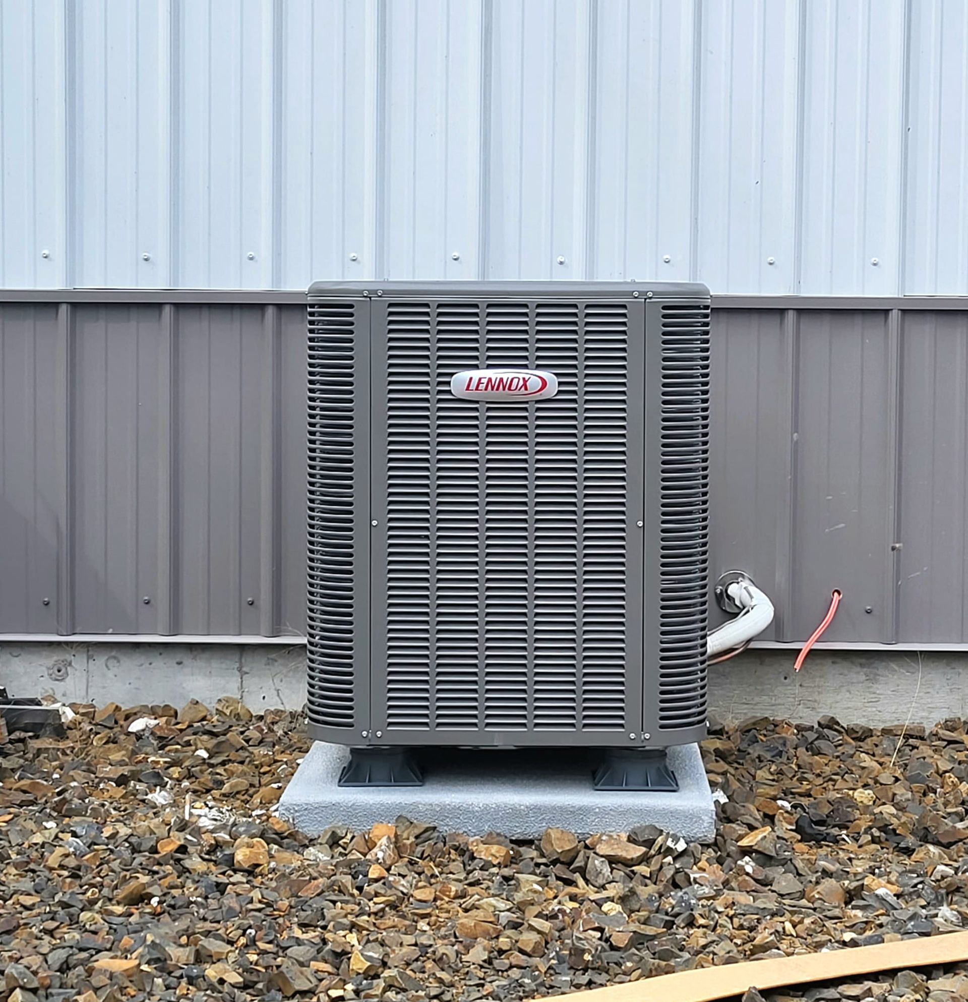 A large air conditioner is sitting on top of a pile of rocks next to a building.