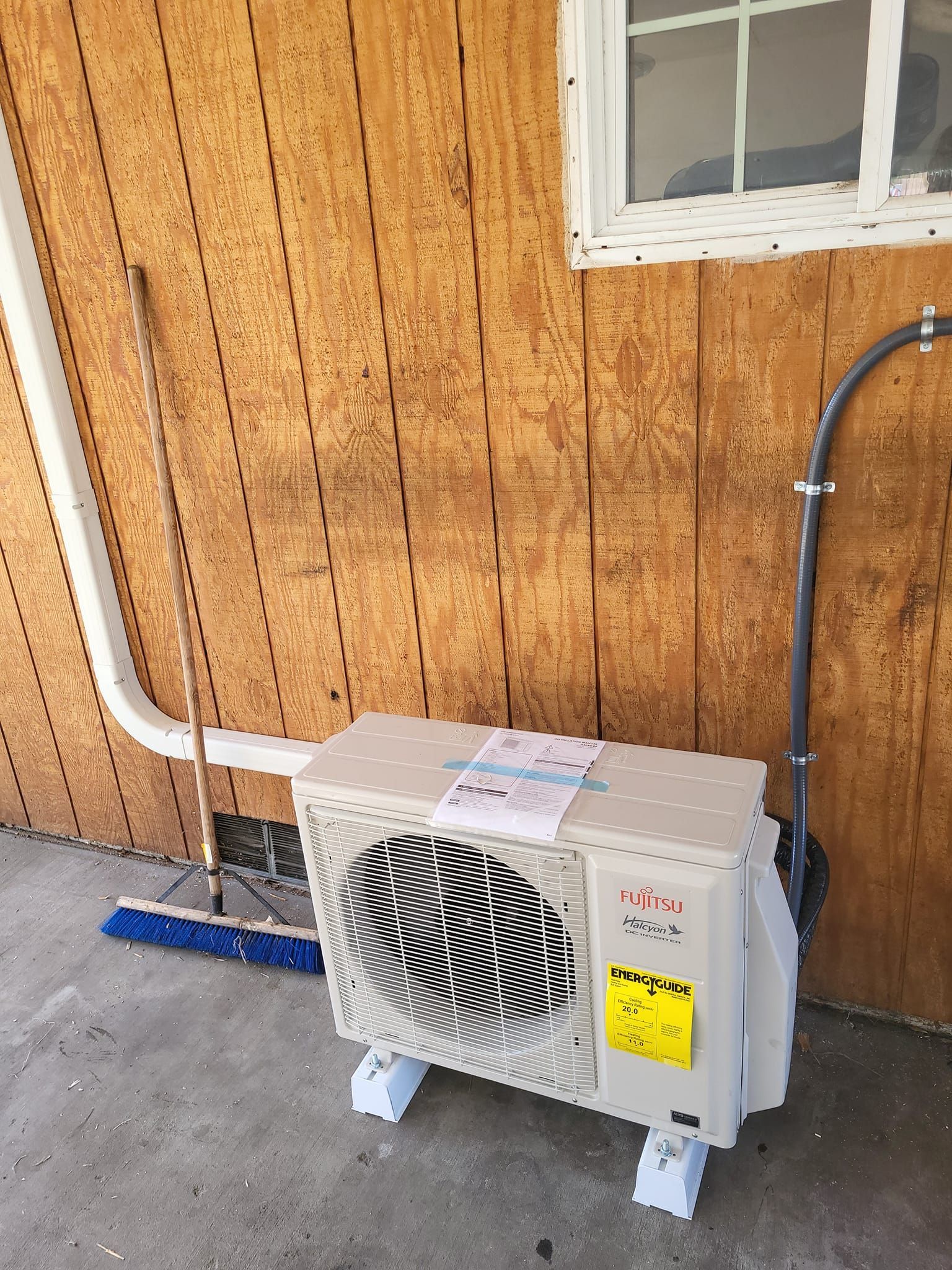 A white air conditioner is sitting outside of a wooden building next to a window.