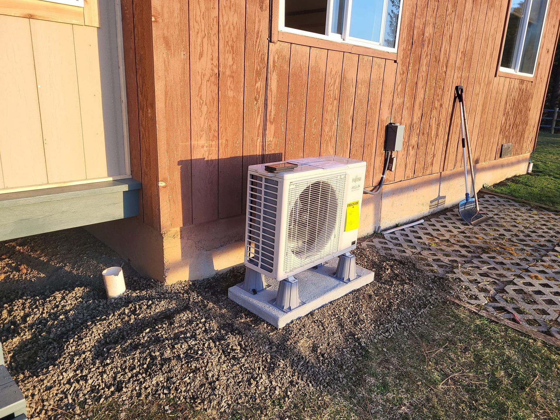 A small air conditioner is sitting outside of a wooden building.