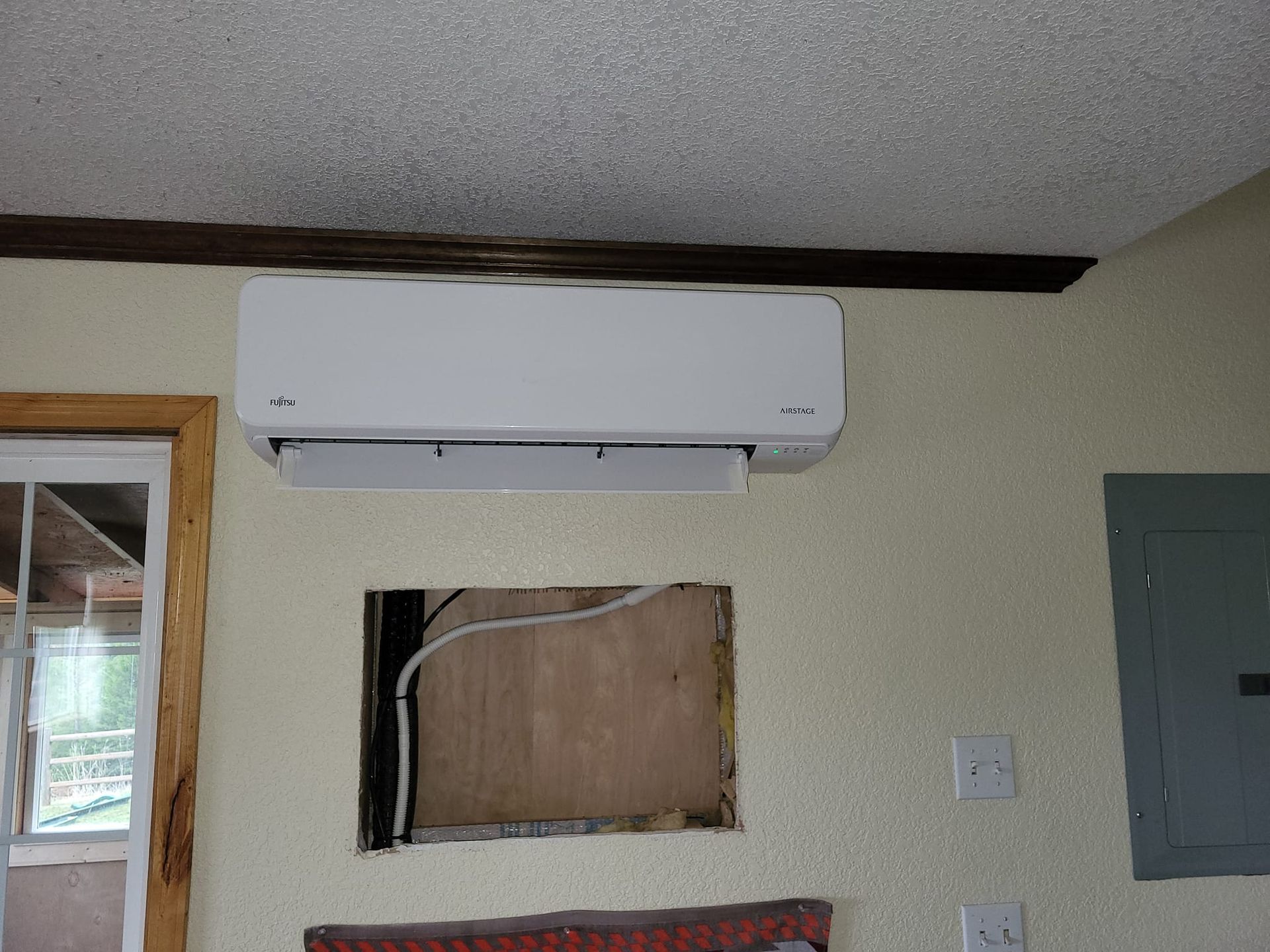 A white air conditioner is mounted on a wall next to a window.