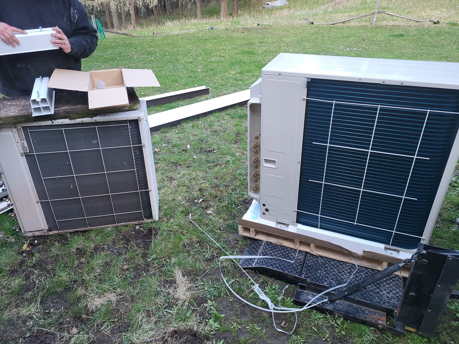 Two air conditioners are sitting on top of a wooden pallet in the grass.