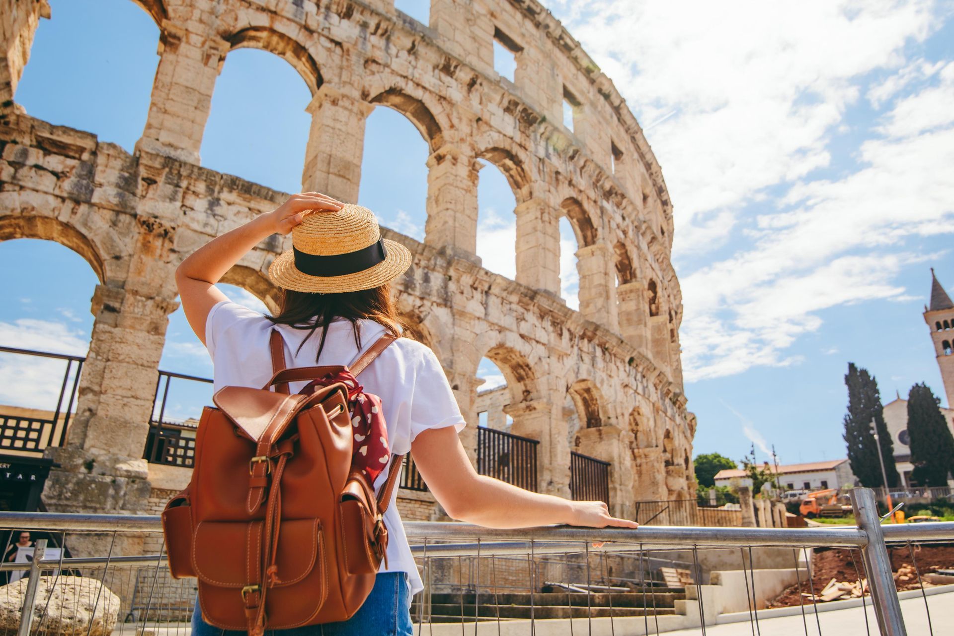 Woman with backpack at the Pula Arena in Croatia, looking at the Roman amphitheater on a sunny day.