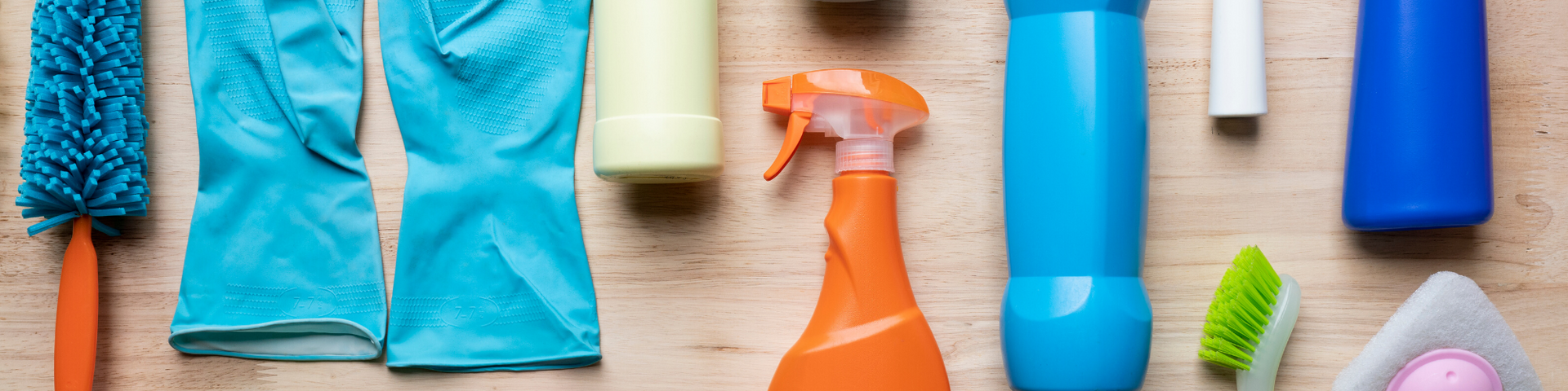 Colorful household cleaning supplies and tools arranged in a row on a wooden surface