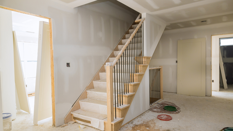 Staircase under construction: light wood steps, black spindles, unfinished walls, open doorway.