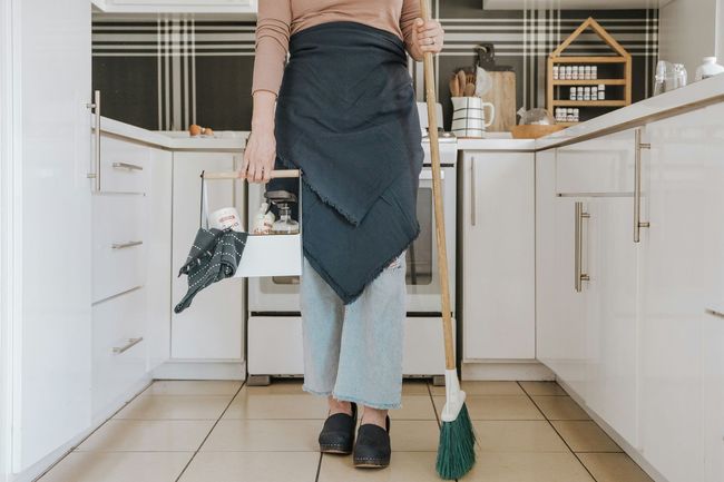 Person in kitchen holding broom and dustpan; cleaning.