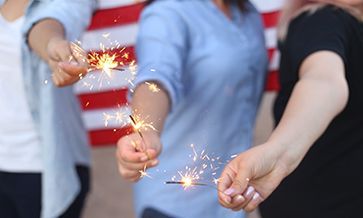A group of people are holding sparklers in their hands in front of an american flag.