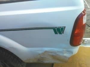 A white truck with a green stripe on the side is parked on the side of the road.