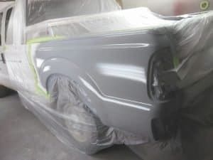 A truck is covered in plastic while being painted in a garage.