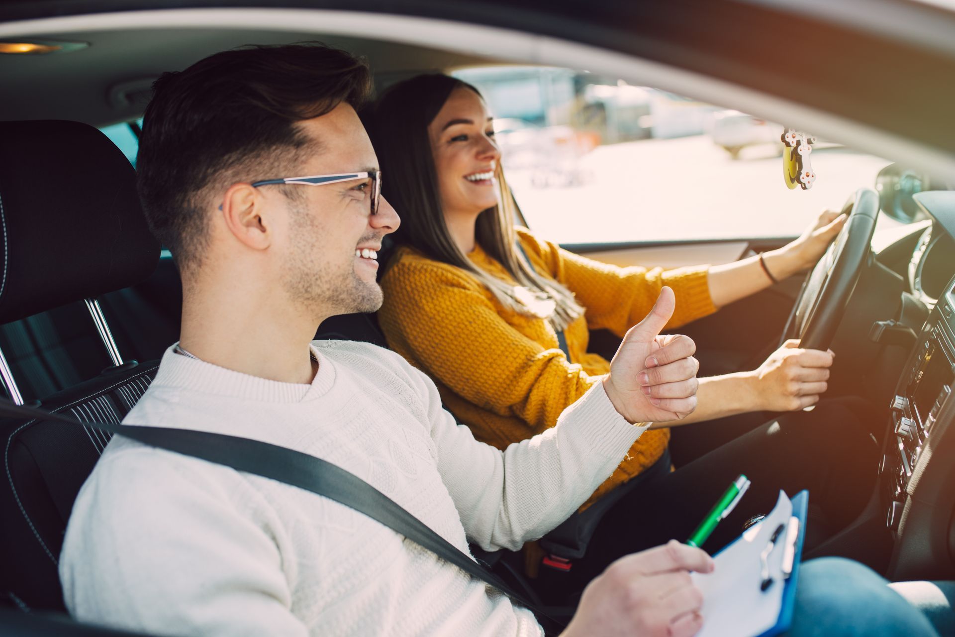 A man and a woman are sitting in a car giving a thumbs up.