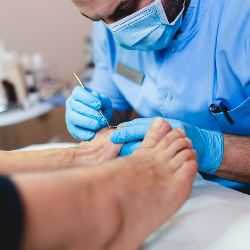 Medical professional in blue gloves and mask treating a patient’s foot with a small instrument