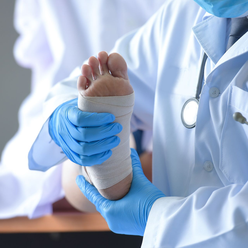 Healthcare worker wrapping a patient's foot with a white bandage, wearing blue gloves and a white coat.