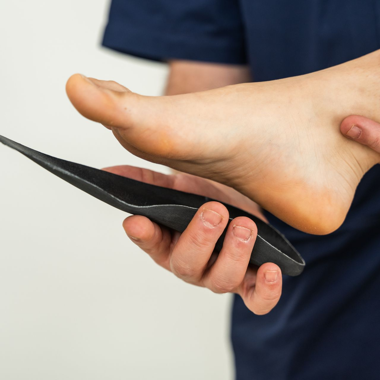 Foot being examined with a black insole in hand, suggesting a foot support fitting.