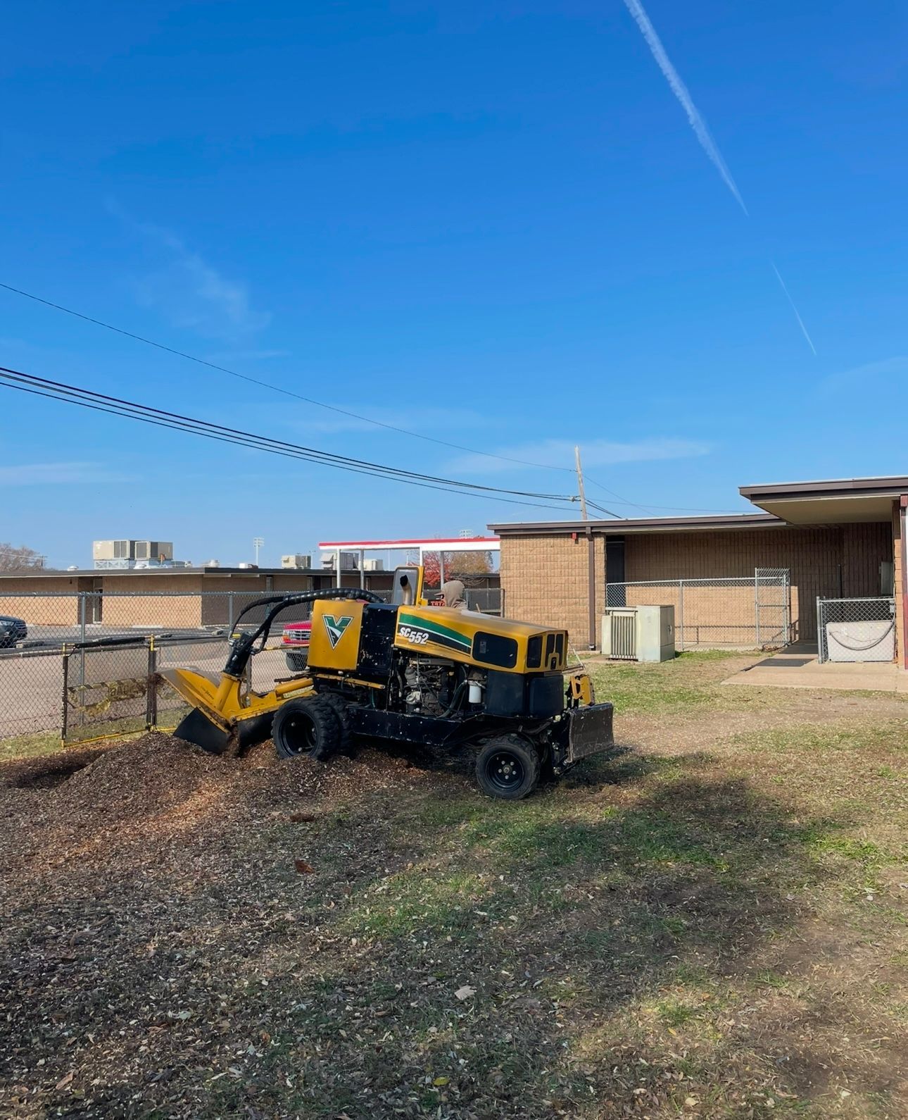 A yellow and black stump grinder is sitting in a field next to a building.