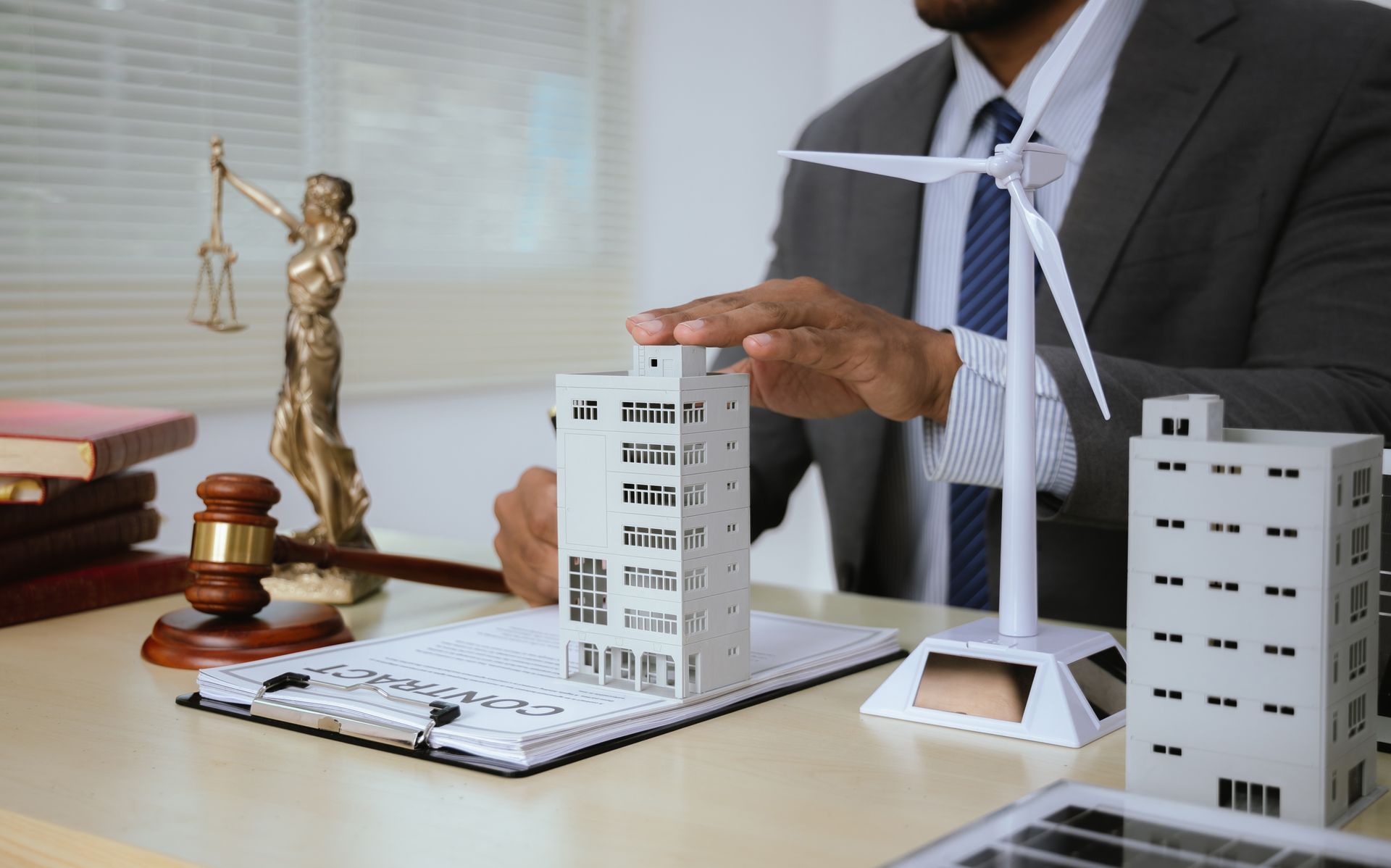 Businessman reviewing scale model buildings and wind turbine on office desk with scales of justice.