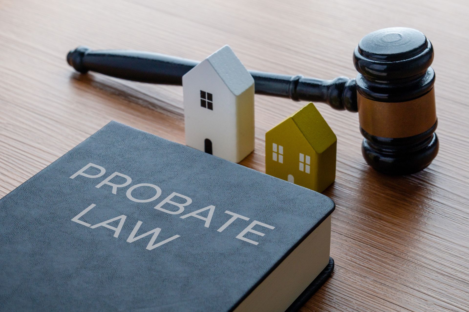 Probate law book beside a gavel and small houses on a wooden desk