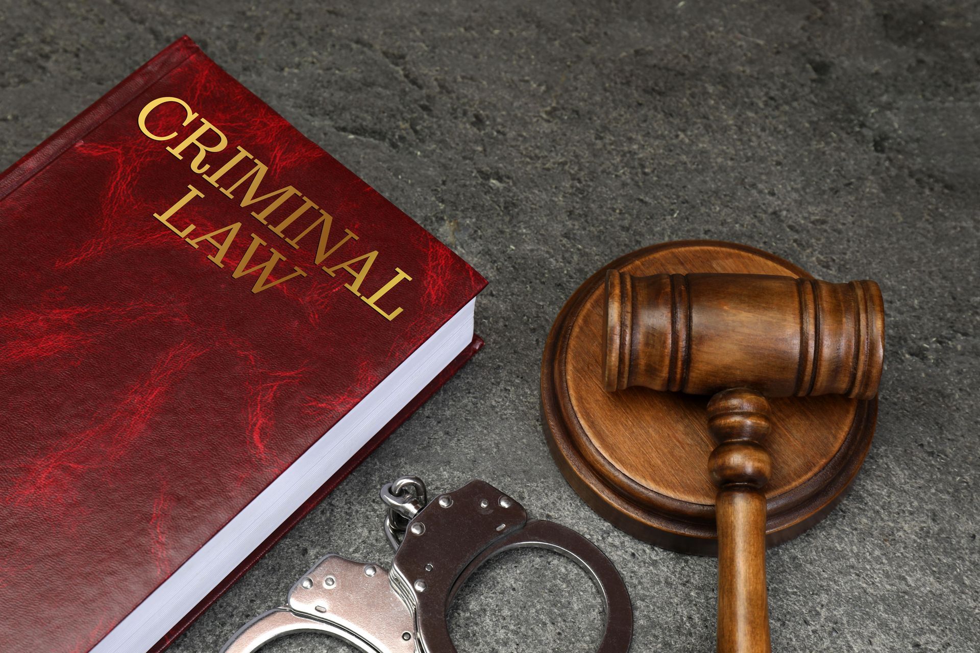 Red criminal law book beside a wooden gavel and handcuffs on dark surface