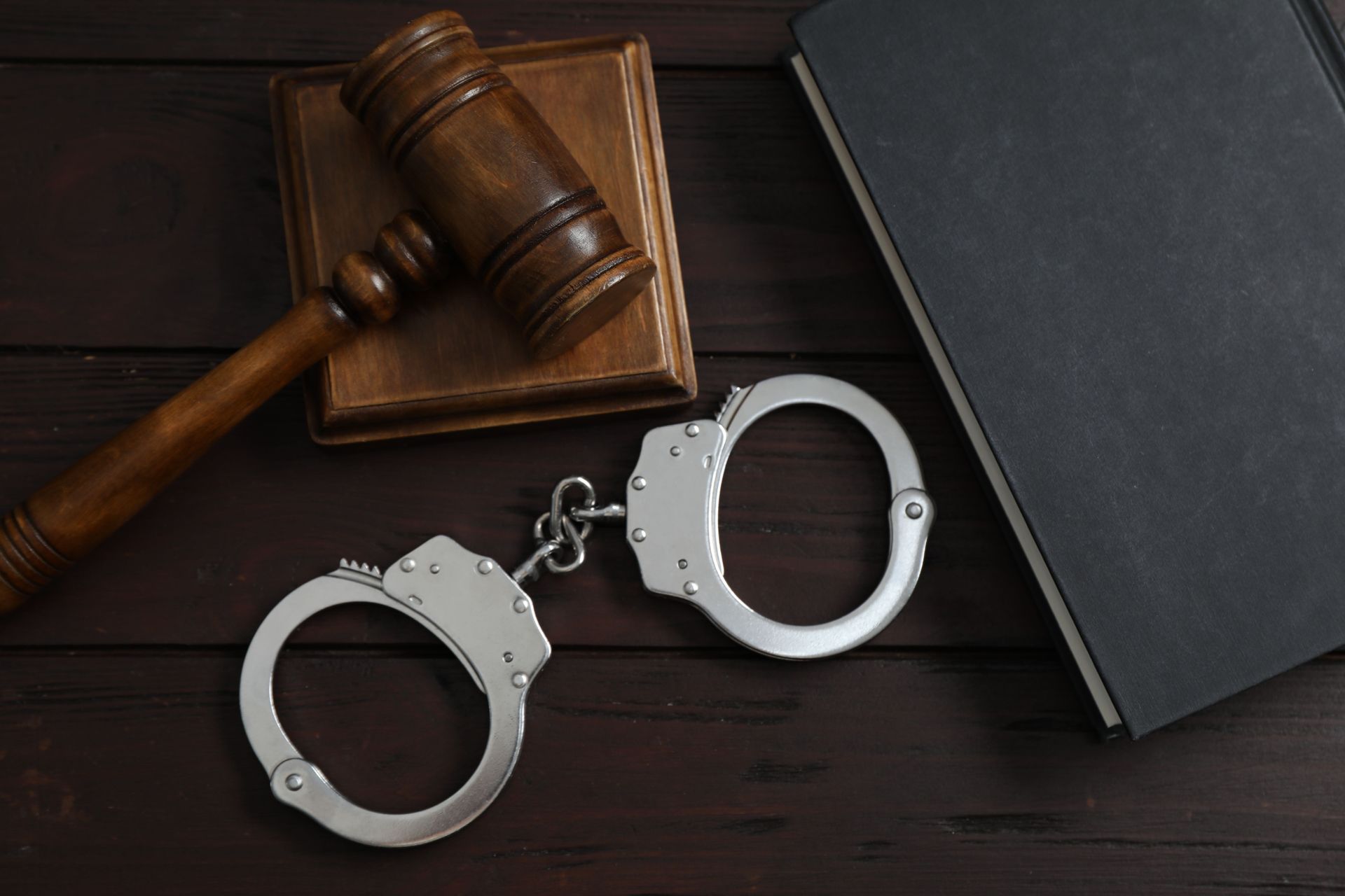Handcuffs beside a judge’s gavel on a dark desk next to a closed black folder