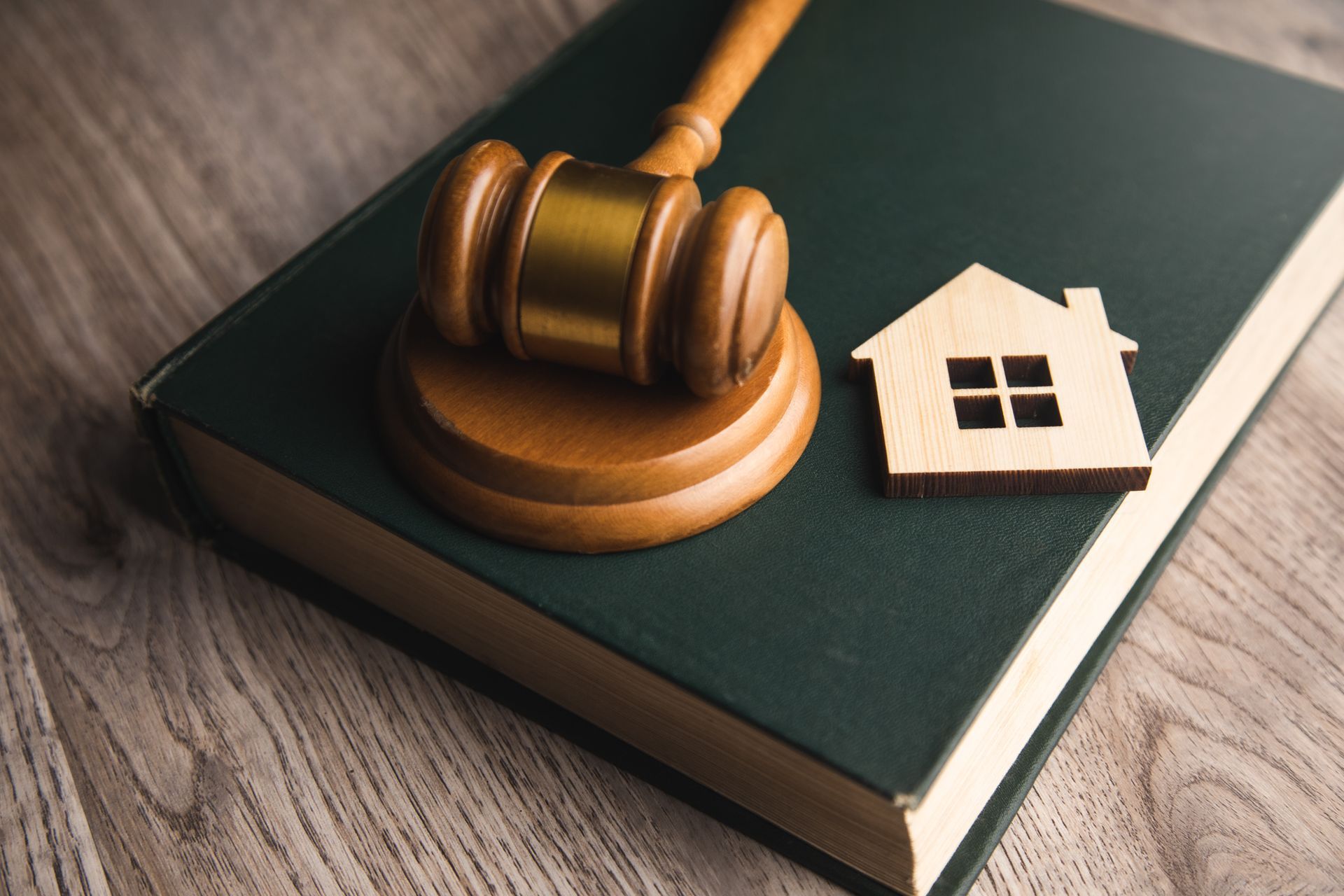 Wooden gavel beside a small house model on a dark book, suggesting property or legal matters