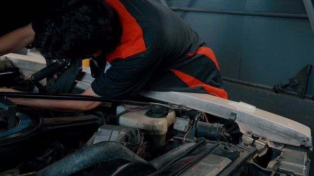 Mechanic in orange and black uniform working under a car hood in a garage | A-Tech Auto Repair