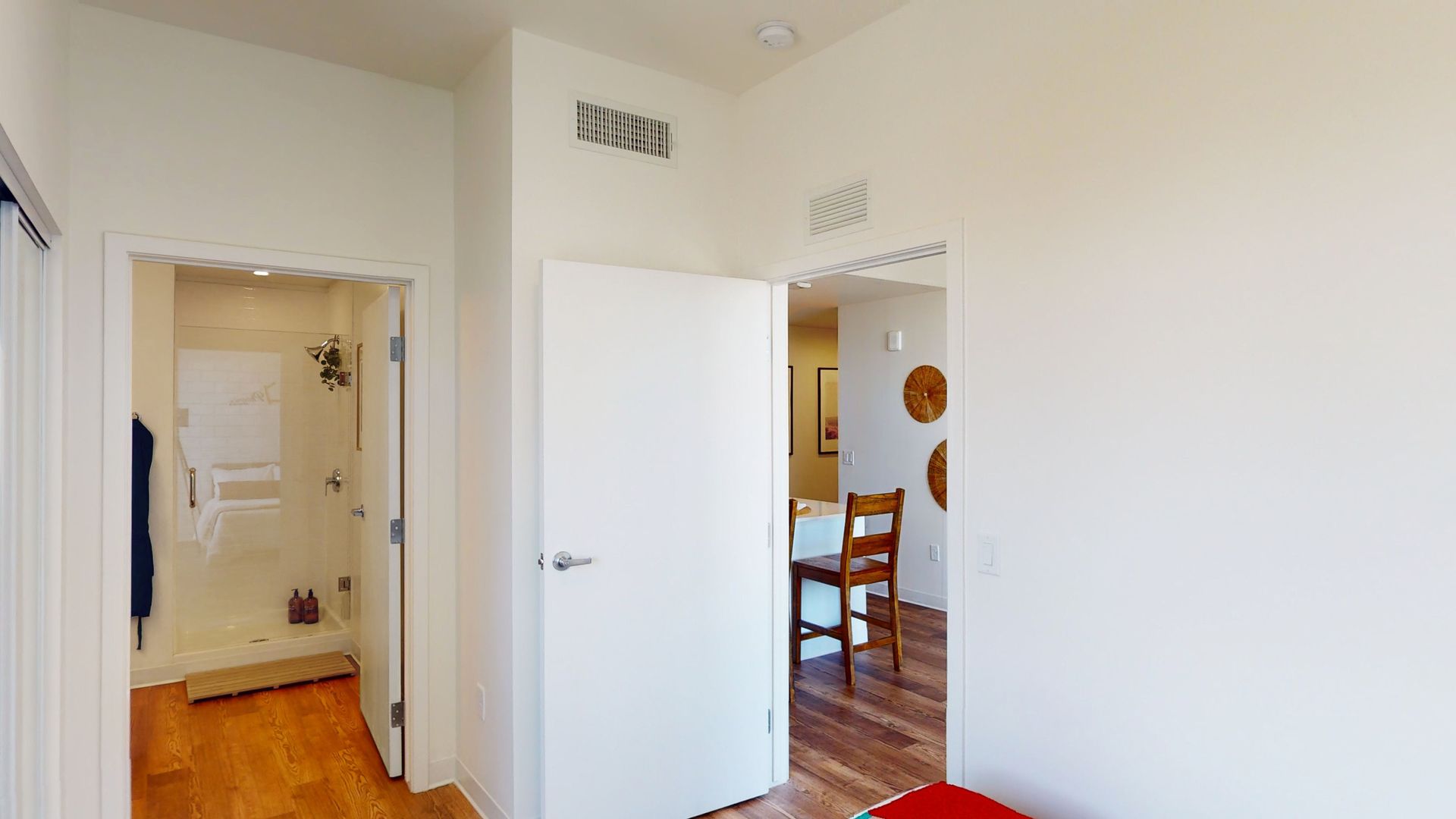 A bedroom with hardwood floors , a bed , a bathroom and a dining room.