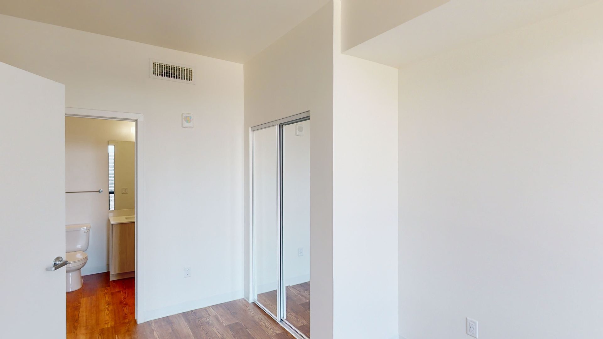 A bedroom with a toilet , closet , and mirror.