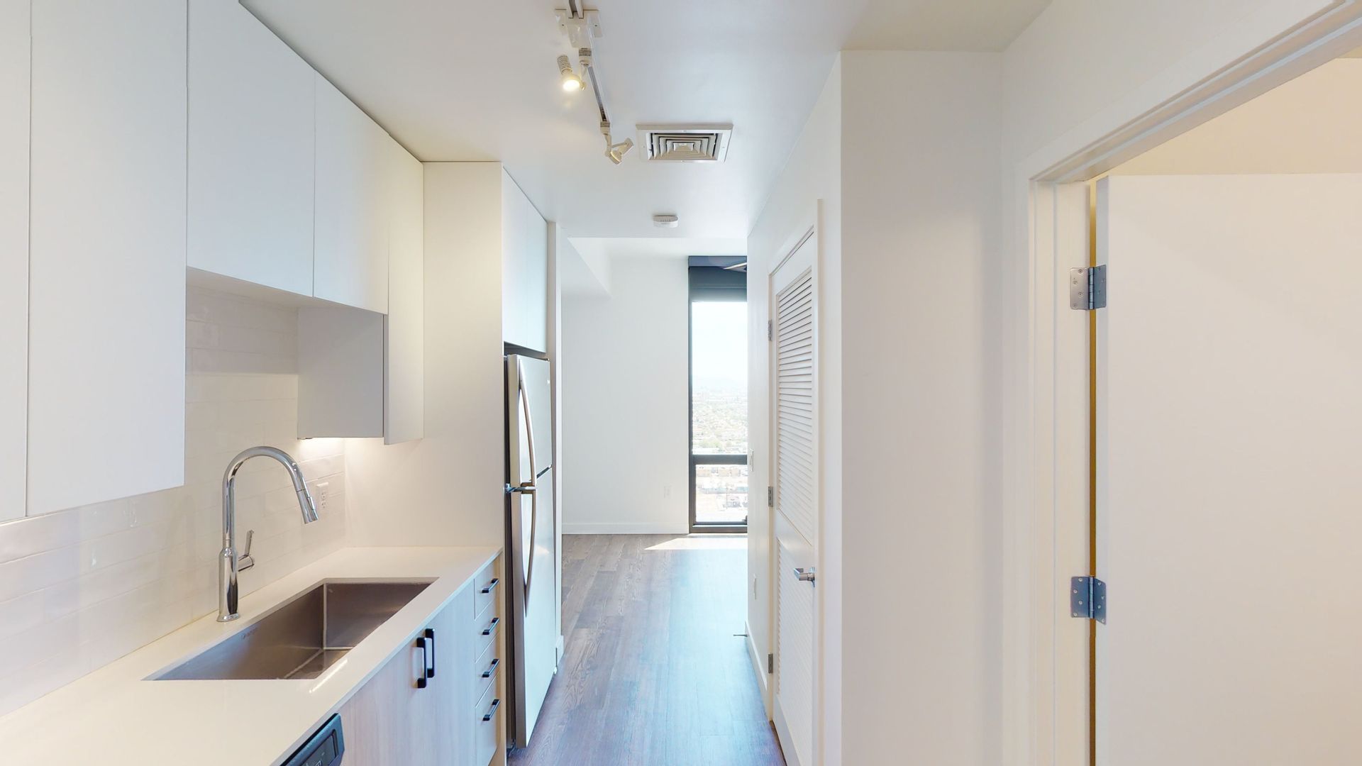 A kitchen with a sink , refrigerator , and dishwasher in a hallway.