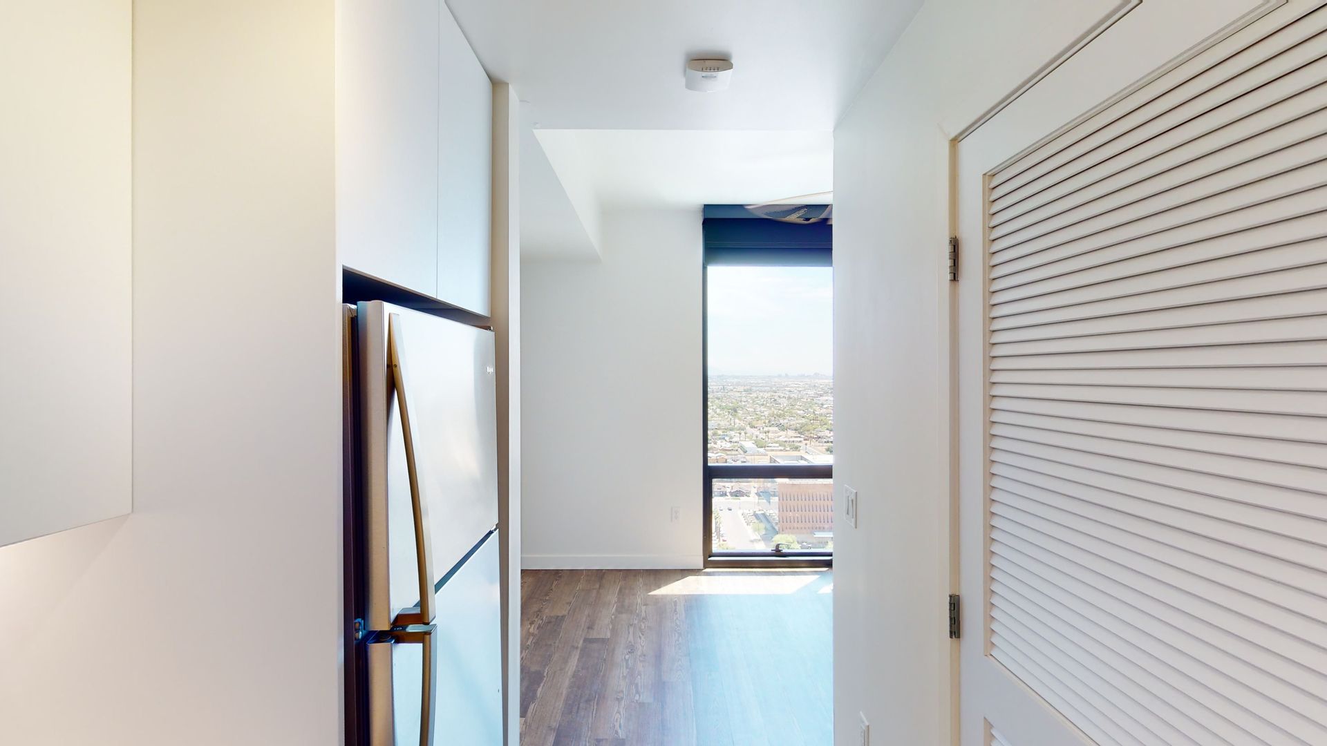 A hallway in a house with a refrigerator and a window.