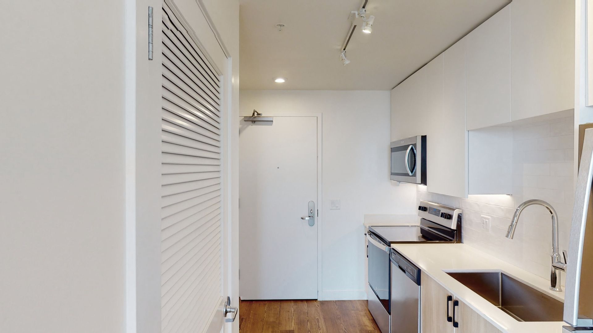A kitchen with white cabinets , stainless steel appliances , a sink , and a microwave.