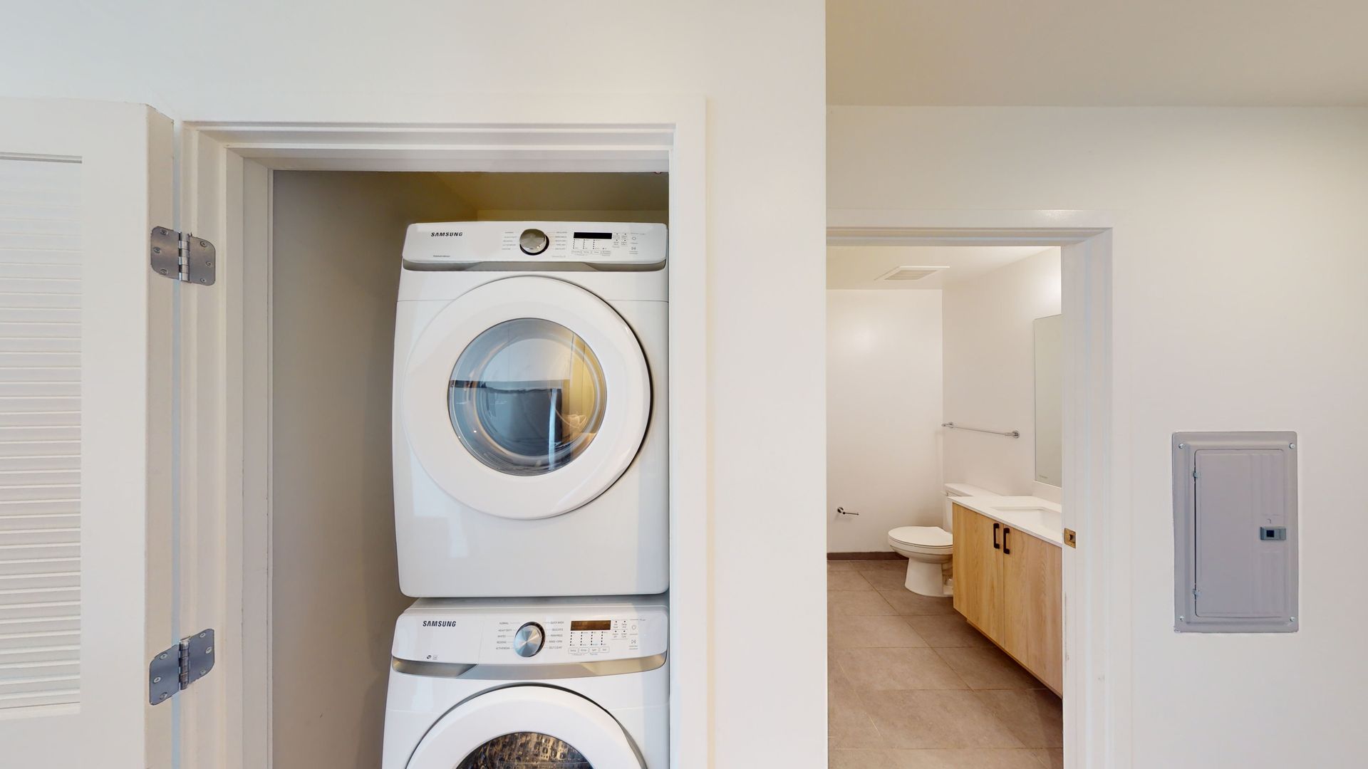 A washer and dryer are stacked in a closet next to a bathroom.