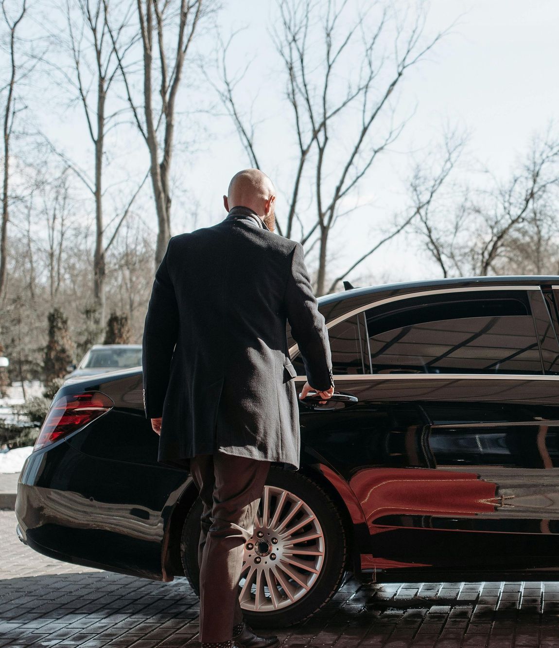 A man in a black coat is standing next to a black car.