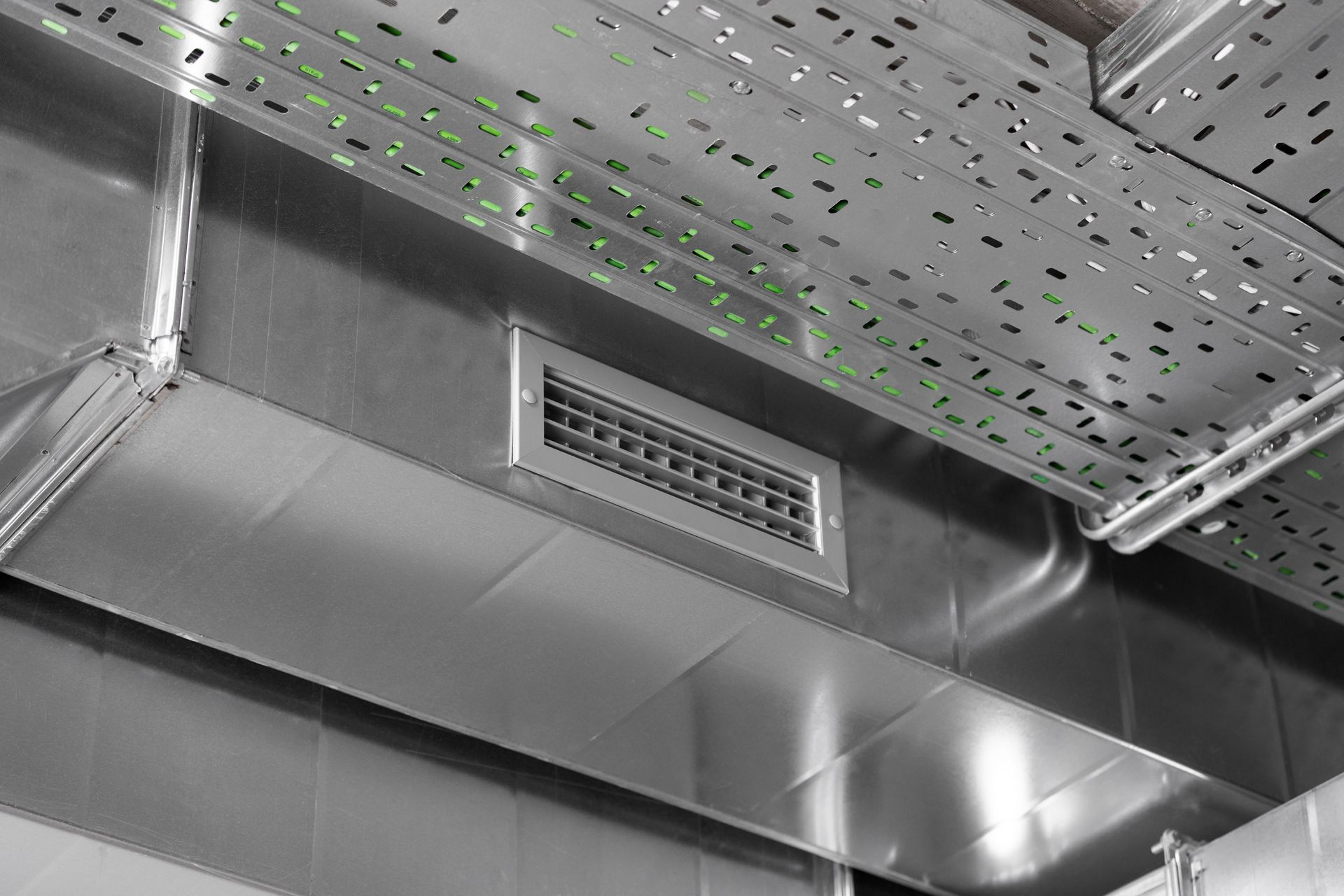 Metal ventilation duct with air vent and perforated ceiling, industrial setting.