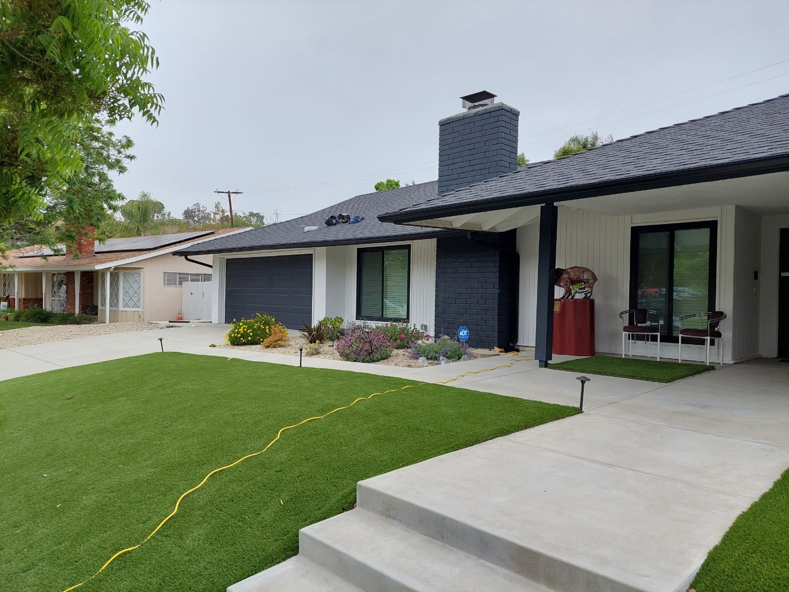 A white house with a black roof and a large lawn in front of it.