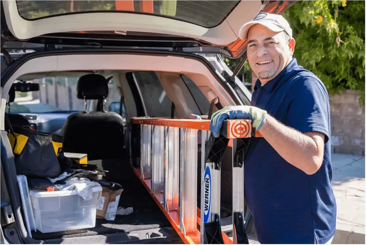 A man is carrying a ladder out of the back of a car.