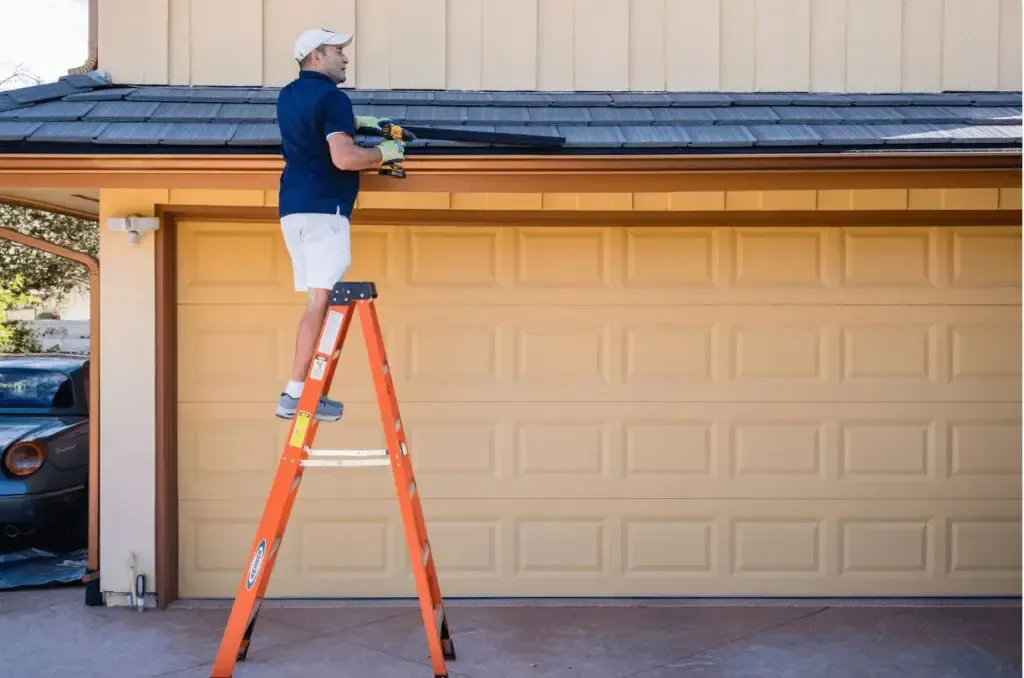 A man is standing on a ladder in front of a garage door.