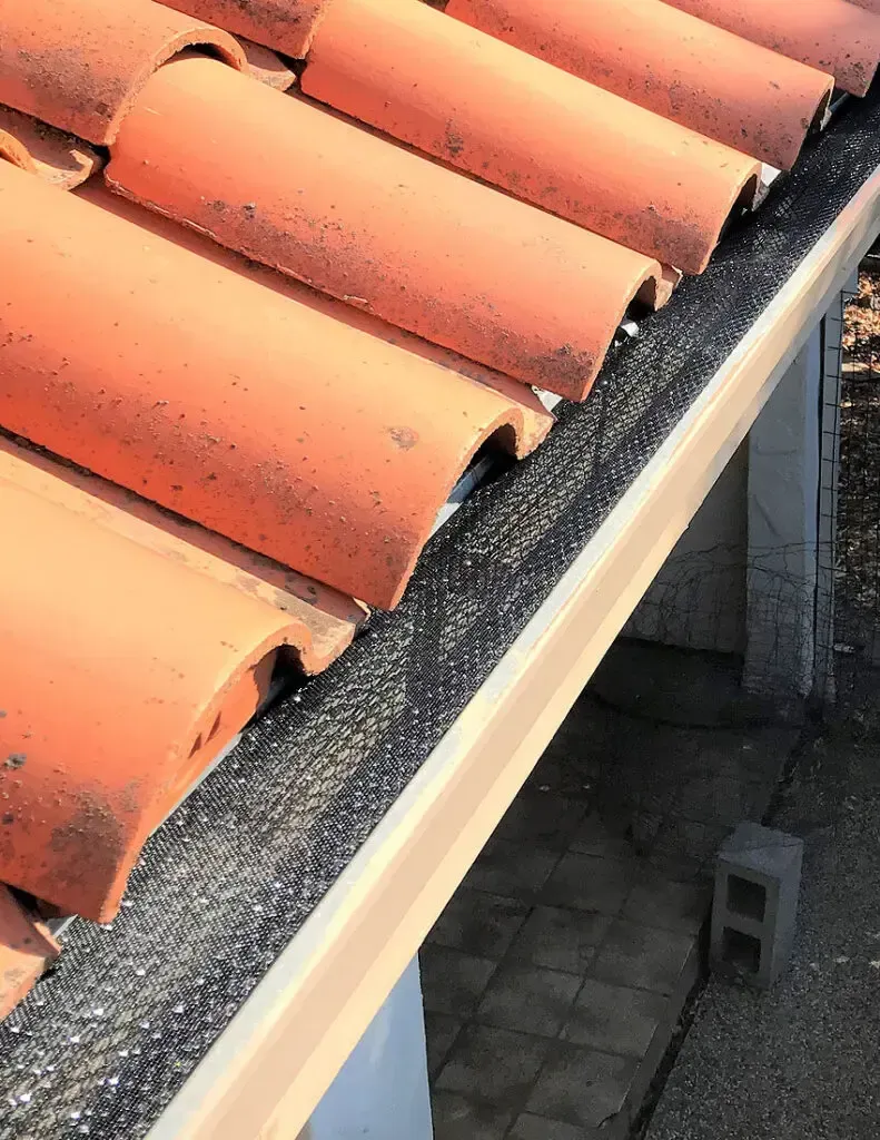 A close up of a gutter on a roof with red tiles