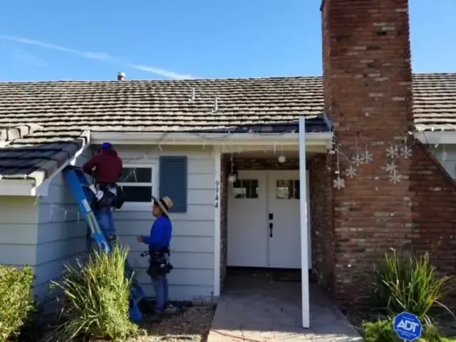 A man on a ladder is working on the roof of a house